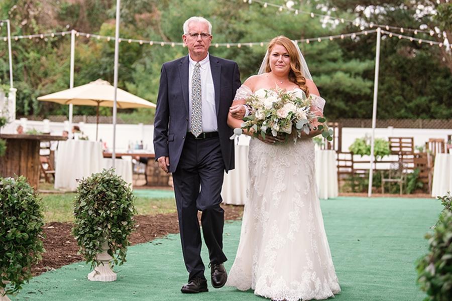 Father walking daughter down the isle on her wedding day while holding her wedding bouquet